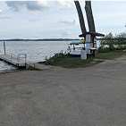 A photo of a floating pier next to a boat ramp, and to the left of the pier there is two big racks filled with colorful kayaks and kanoes